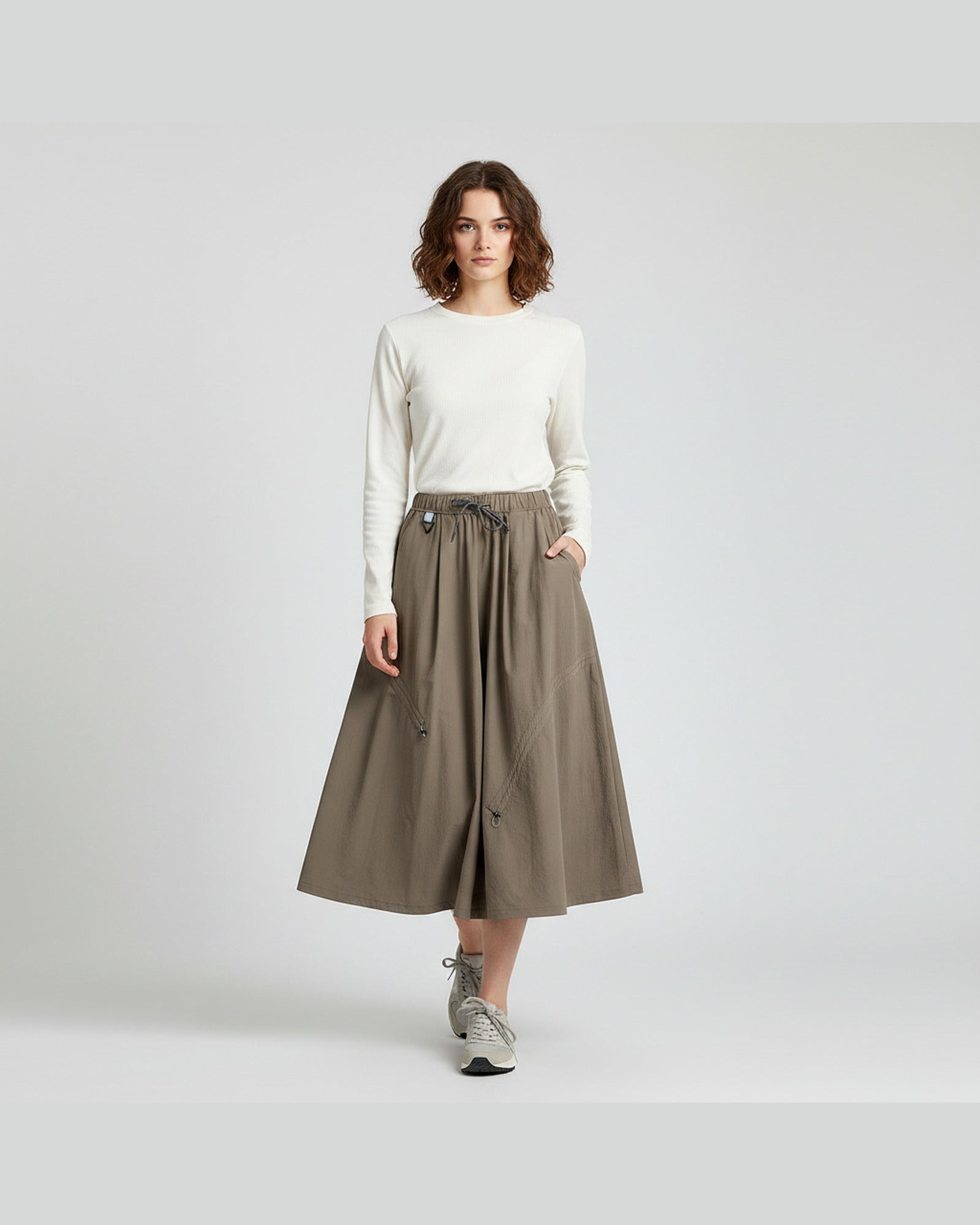 Model in mocha brown technical cargo skirt with curved seam detail and drawstring hem, studio outdoor style