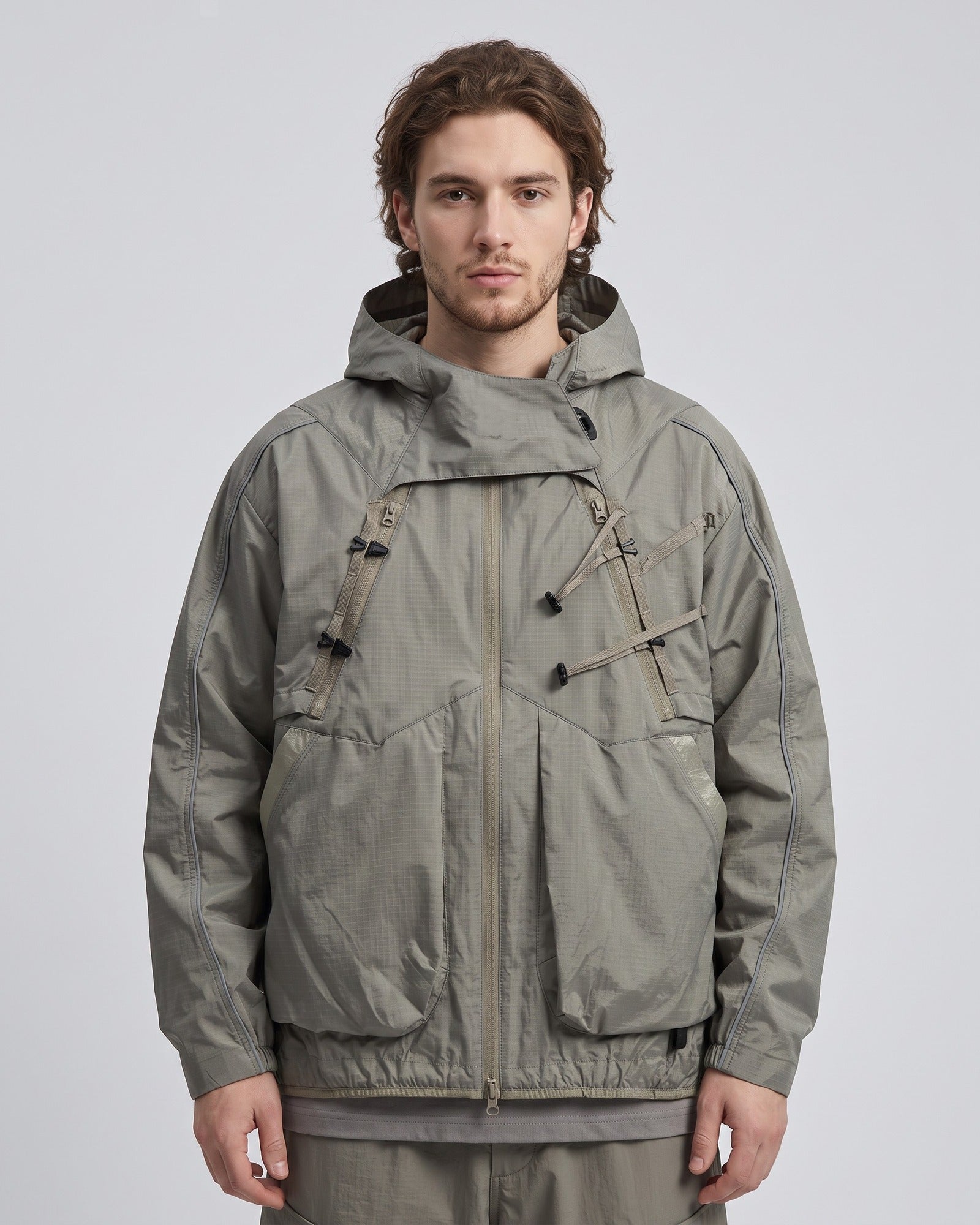 Sandstone Khaki 2-in-1 detachable hooded shell jacket on male model, outdoor techwear, X-webbing buckles and reflective trims, light-grey studio