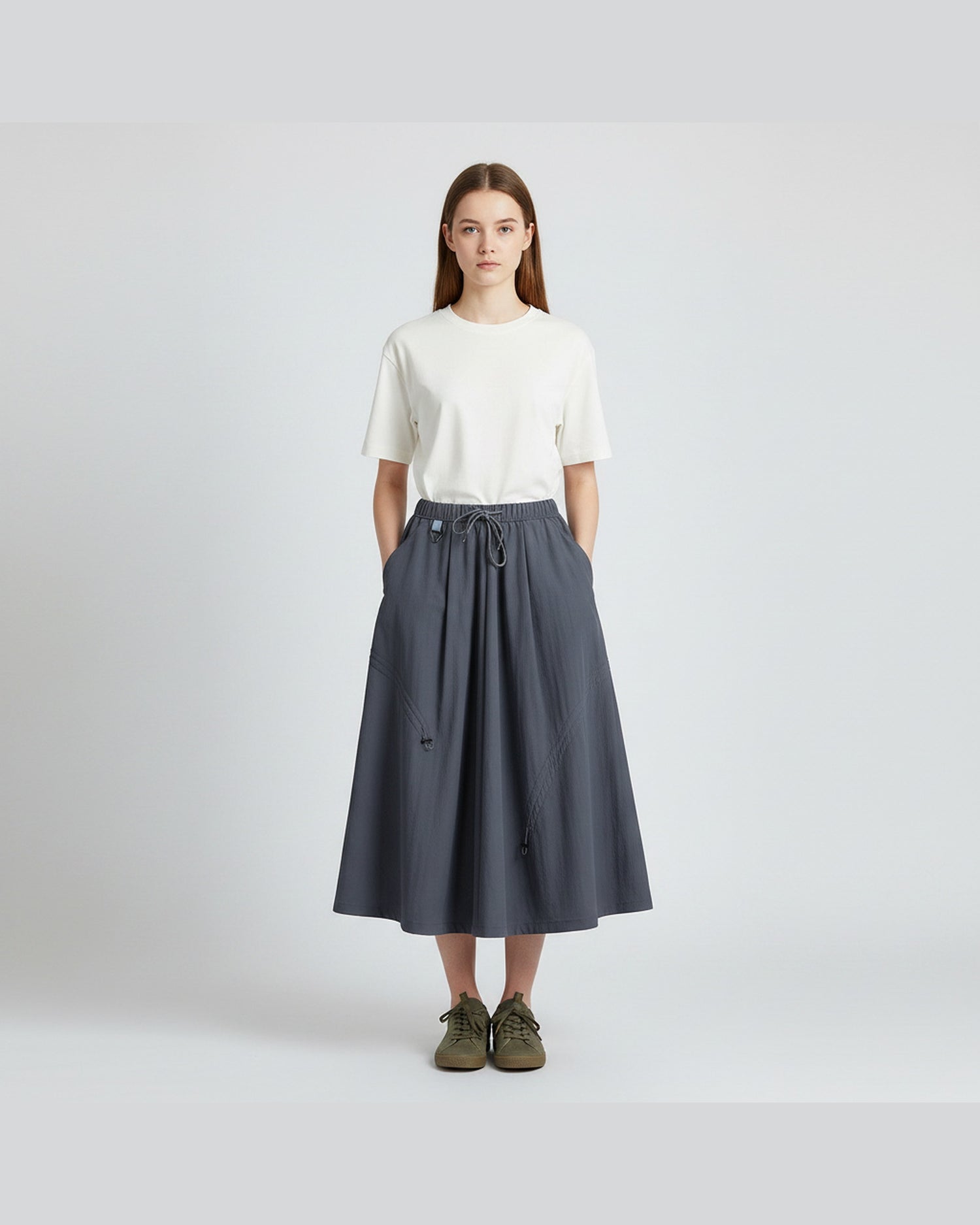 Model in ink blue technical A-line cargo skirt with drawstring waist, clean light-grey studio background