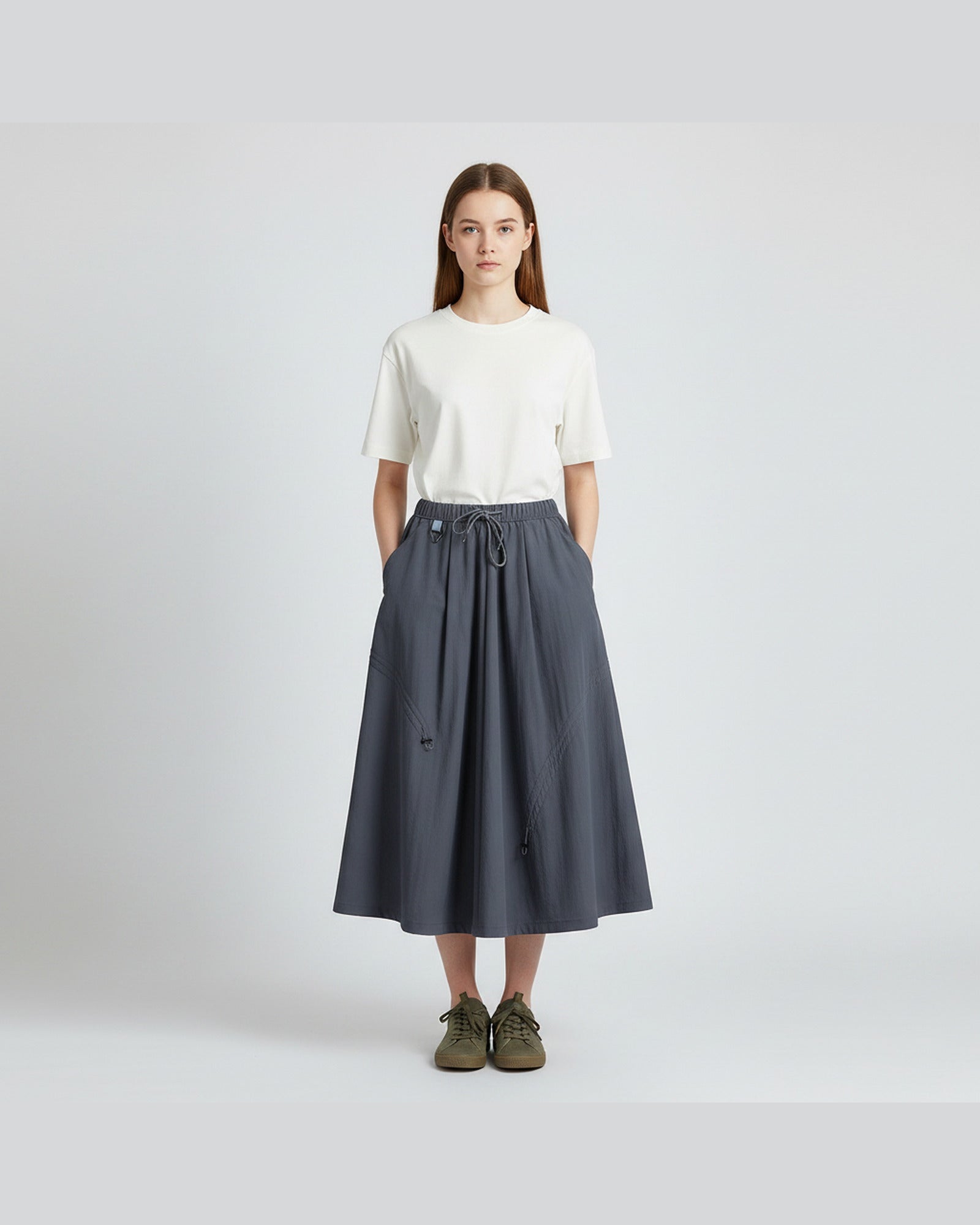 Model in ink blue technical A-line cargo skirt with drawstring waist, clean light-grey studio background