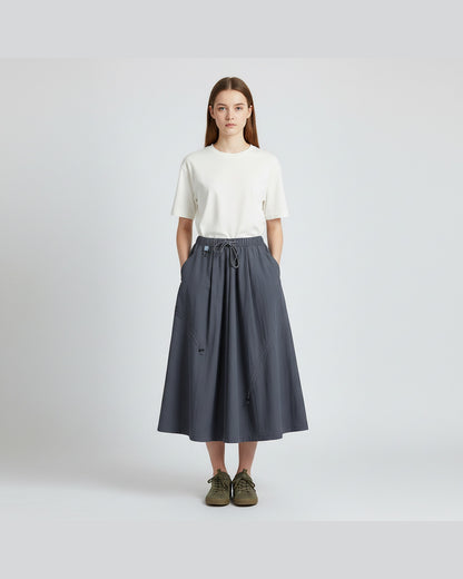 Model in ink blue technical A-line cargo skirt with drawstring waist, clean light-grey studio background