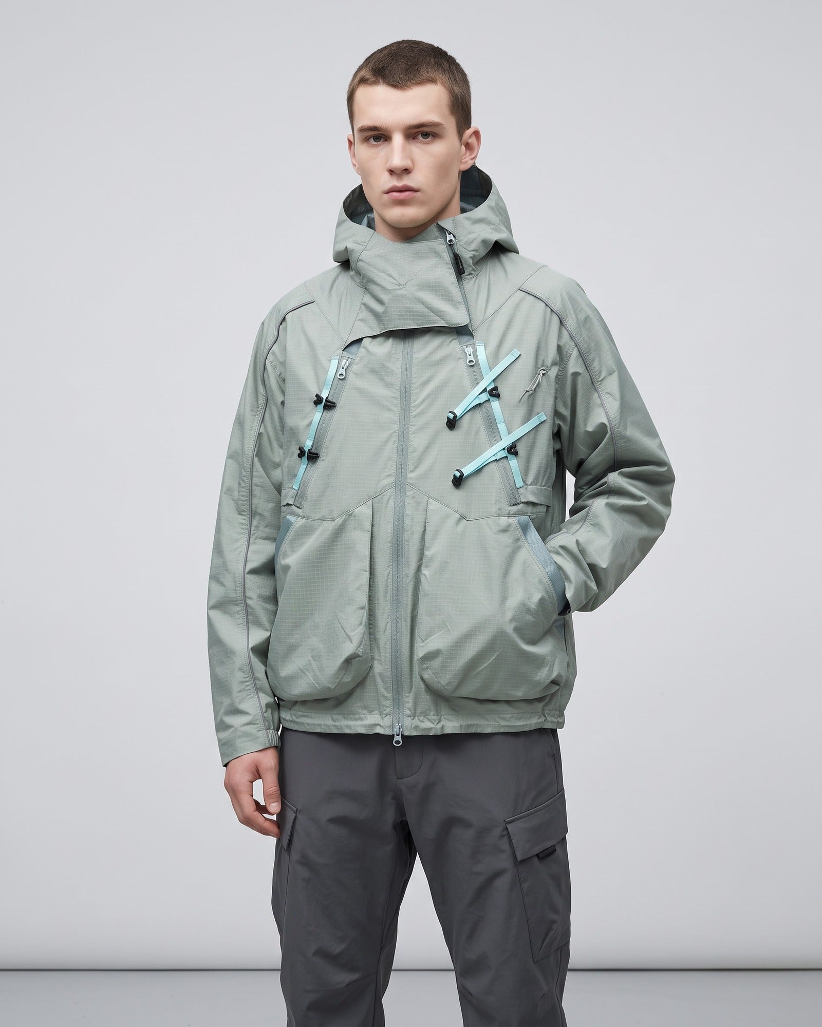 Bamboo Green 2-in-1 detachable hooded shell jacket on male model with teal webbing buckles, technical outdoor techwear studio shot